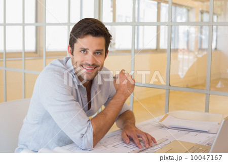 Smiling businessman working on blueprints in office 10047167