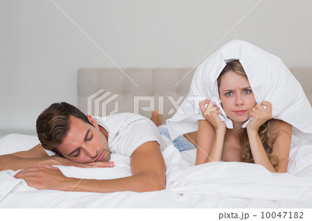 Angry woman holding pillow besides a sleeping man in bed Angry woman holding pillow besides a sleeping man in bed 10047182