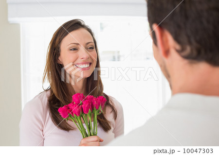 Cheerful woman looking at man with flowers 10047303
