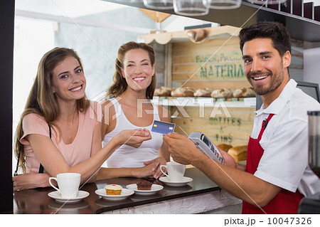 Friends with woman holding out credit card at coffee shop Friends with woman holding out credit card at coffee shop 10047326