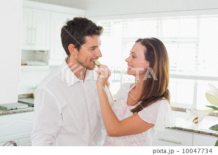Loving woman feeding man cucumber slice in kitchen Loving woman feeding man cucumber slice in kitchen 10047734