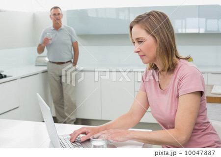 Woman using laptop while man drinking water in kitchen Woman using laptop while man drinking water in kitchen 10047887