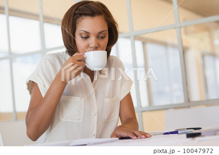 Businesswoman drinking coffee while working on blueprint in offi Businesswoman drinking coffee while working on blueprint in offi 10047972