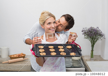 Man kissing woman's cheek as she holds freshly baked cookies in Man kissing woman's cheek as she holds freshly baked cookies in 10048012