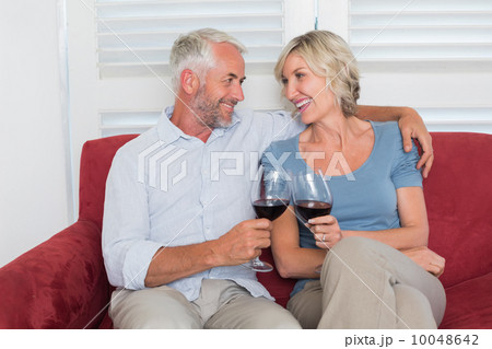 Relaxed mature couple toasting wine glasses in living room 10048642