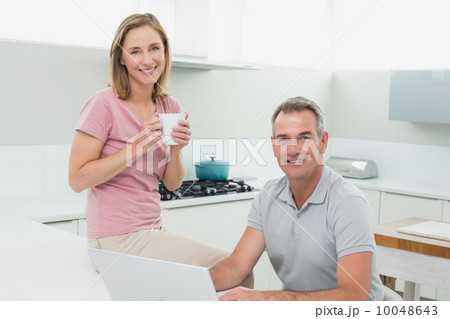 Portrait of a happy couple using laptop in kitchen 10048643