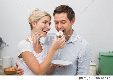 Happy woman feeding man pastry in kitchen 10048737