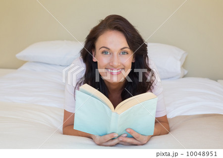 Woman holding book while lying in bed 10048951