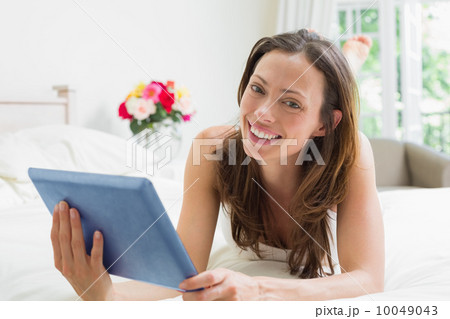 Smiling relaxed woman using digital tablet in bed 10049043