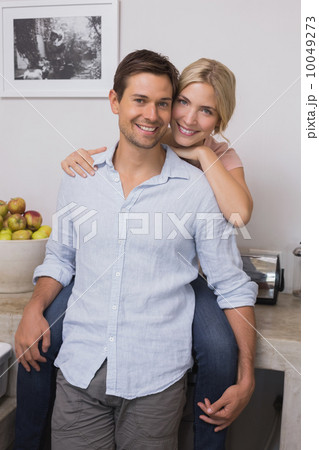 Smiling woman embracing man from behind at home 10049273