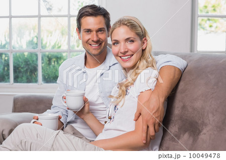 Relaxed loving couple with coffee cups sitting on sofa Relaxed loving couple with coffee cups sitting on sofa 10049478