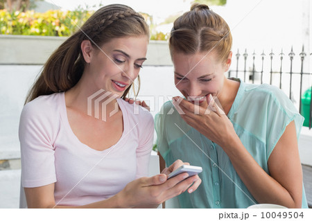 Happy female friends reading text message at coffee shop 10049504