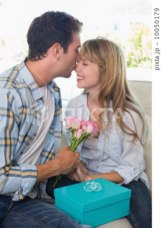 Young man kissing woman with flowers and gift box Young man kissing woman with flowers and gift box 10050179