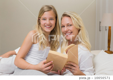 Mother and daughter holding story book in bed 10050571