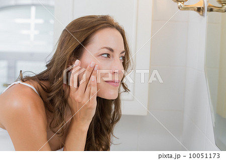 Side view of a beautiful young woman examining her face Side view of a beautiful young woman examining her face 10051173