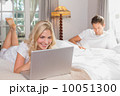 Woman using laptop while man reading book in bed 10051300