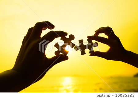 Two hands trying to connect puzzle pieces with sunset background 10085235