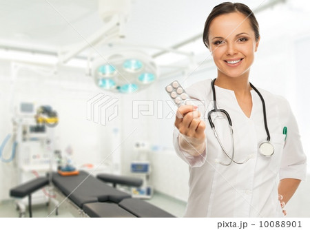 Young positive brunette doctor woman holding pills in surgery room interior Young positive brunette doctor woman holding pills in surgery room interior 10088901