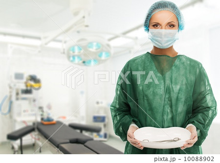 Young woman doctor in cap and face mask holding medicine tray with surgery tools 10088902
