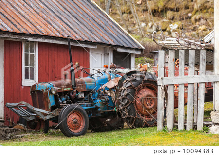 Old farm tractor stands in Norwegian village nearby red wooden house Old farm tractor stands in Norwegian village nearby red wooden house 10094383