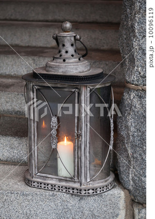 Old metal outdoor lamp with burning candle stands on stone stair 10096119