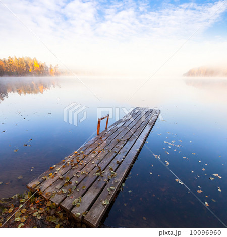 Small wooden pier on still lake in bright autumnal foggy morning Small wooden pier on still lake in bright autumnal foggy morning 10096960