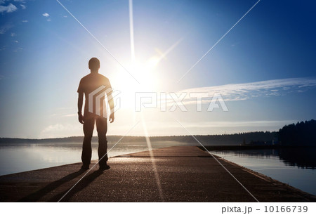 A man stands on the concrete pier starring at the setting Sun 10166739