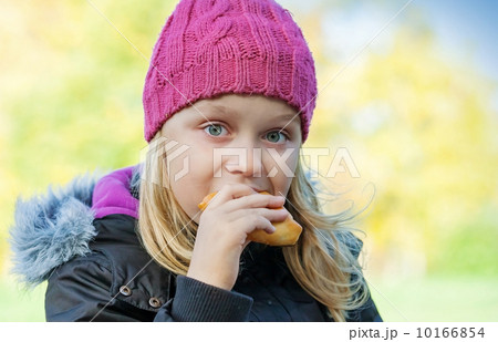 little beautiful blond girl eating cake in autumnal park. Outdoor portrait. 10166854