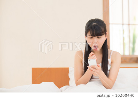 ベッドでスマートフォンを持つ女性 10200440