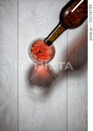 Red wine pouring into glass from bottle on white wooden table. T Red wine pouring into glass from bottle on white wooden table. T 10258799