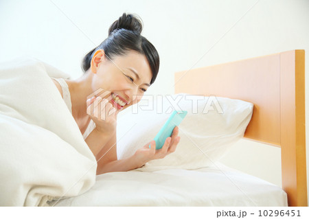 ベッドに入りながらスマートフォンを使う女性 ベッドに入りながらスマートフォンを使う女性 10296451