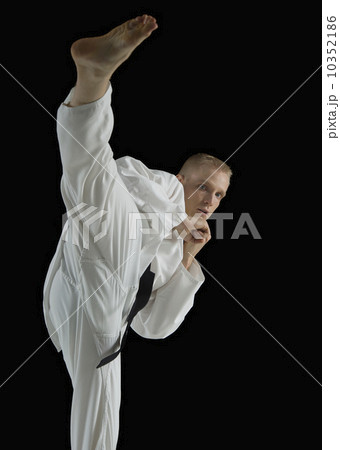 Young man performing karate kick on black background 10352186