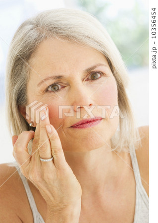 Portrait of senior woman applying moisturizer 10356454