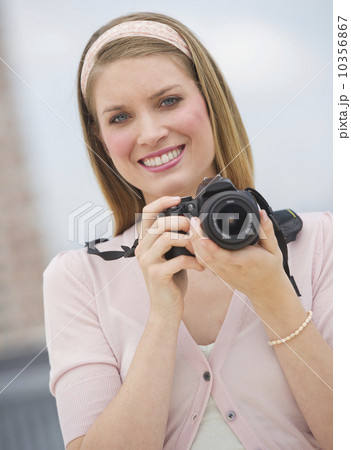 Portrait of young woman holding camera, smiling 10356867