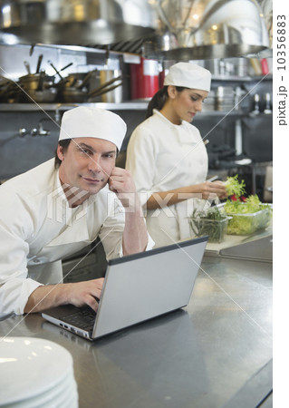 Chef using laptop and cook preparing food in commercial kitchen 10356883