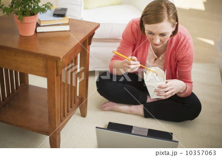 USA, New Jersey, Jersey City, woman sitting on floor, using laptop and eating take out food USA, New Jersey, Jersey City, woman sitting on floor, using laptop and eating take out food 10357063