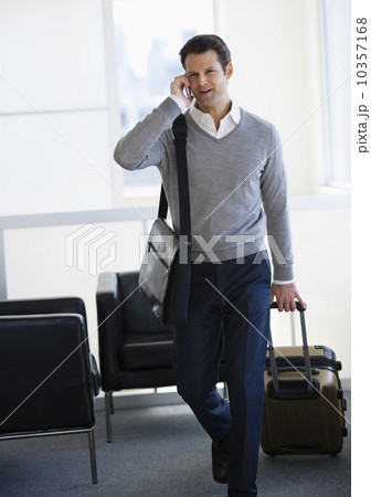 Businessman pulling suitcase and talking on mobile phone in airport lounge 10357168