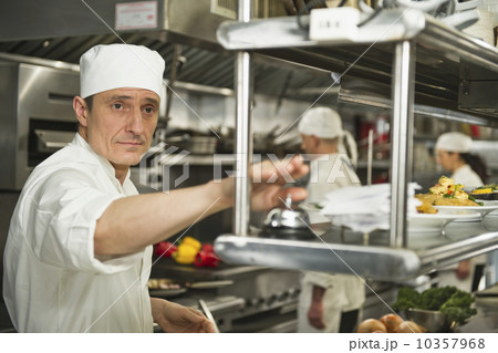 Chef ringing service bell, in background chefs preparing food Chef ringing service bell, in background chefs preparing food 10357968