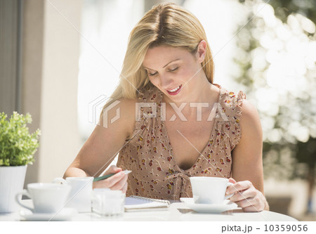 Woman writing journal at outdoor cafe table Woman writing journal at outdoor cafe table 10359056