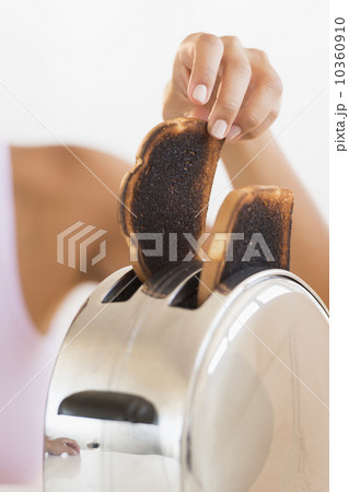 Woman taking burnt toast from toaster 10360910