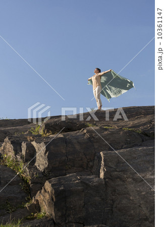 Mature woman standing on cliff with arms raised 10361147