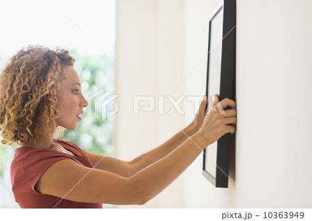 Young woman hanging print on wall 10363949