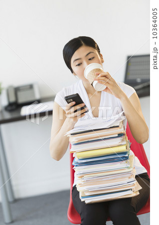 Businesswoman with stack of files texting on phone Businesswoman with stack of files texting on phone 10364005