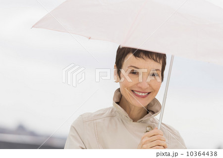 Portrait of smiling woman wearing raincoat and holding umbrella 10364438