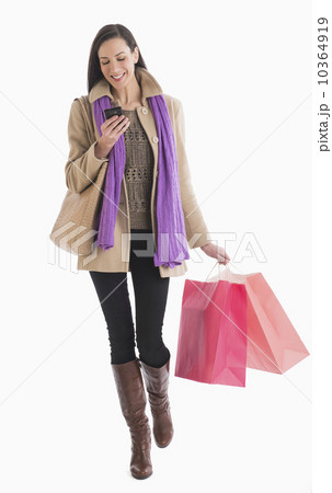 Studio shot of woman carrying shopping bags and text messaging Studio shot of woman carrying shopping bags and text messaging 10364919