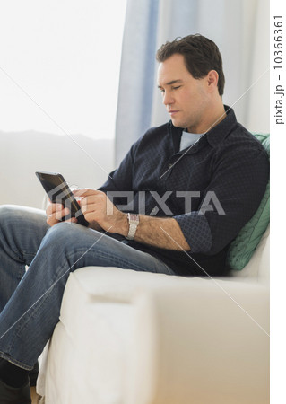 Man sitting on sofa looking at digital tablet 10366361