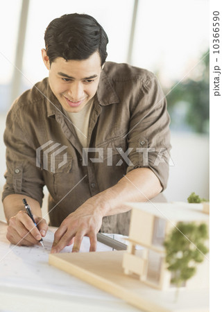 Male architect working with blueprint and model home 10366590