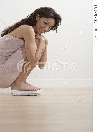 Smiling woman crouching on bathroom scale 10367151