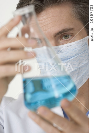 Masked scientist examining blue liquid Masked scientist examining blue liquid 10367703