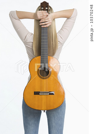 Studio shot of woman holding guitar against her back Studio shot of woman holding guitar against her back 10370248